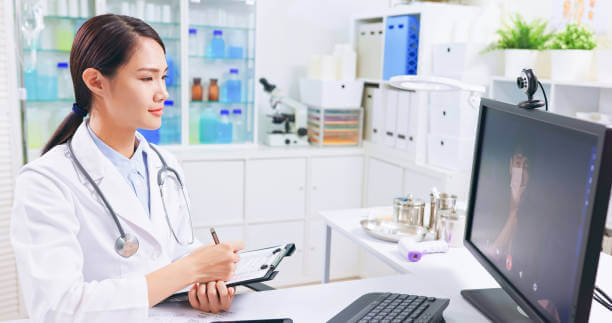 side view of asian female doctor is writing down the notes while talking to patient online through webcam - young man has cough and sore throat