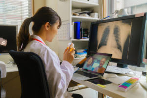 A female doctor is talking with a senior married couple patients online telehealth video call meeting at her office.