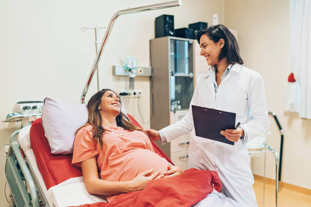 Pregnant woman lying down on a hospital bed and talking to a doctor