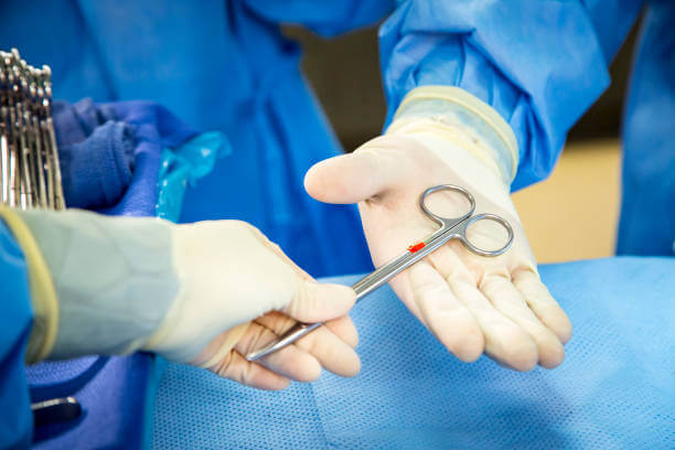 Horizontal image of a gloved hands passing a hemostat during surgery