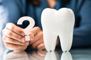 Image of man holding question mark next to a model tooth inquiring about Dental Malpractice Insurance questions.