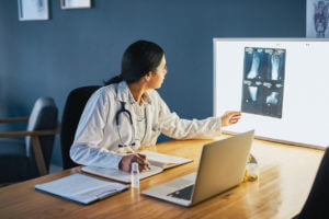 A female Orthopedic Surgeon is looking at an X-ray displayed on her screen.